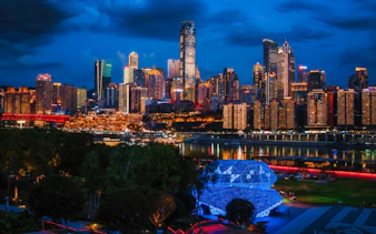 Chongqing skyline at night with illuminated skyscrapers and river view, seen from a park.
