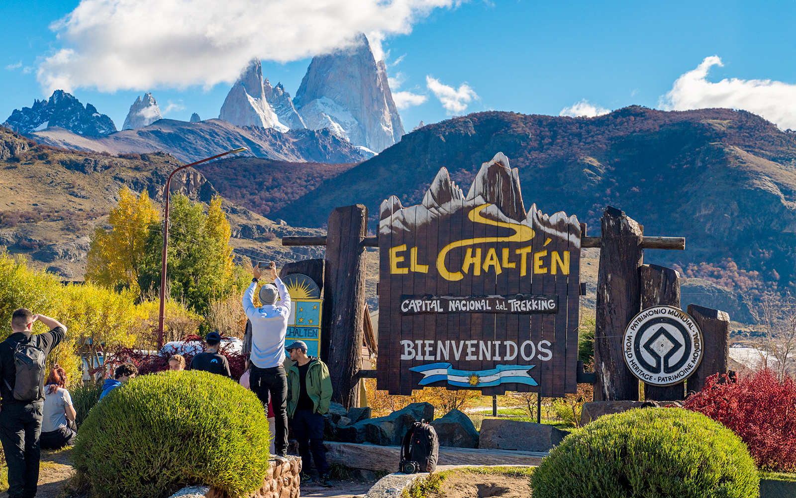 Tourists at El Chaltén welcome sign with mountains in the background, Argentina.