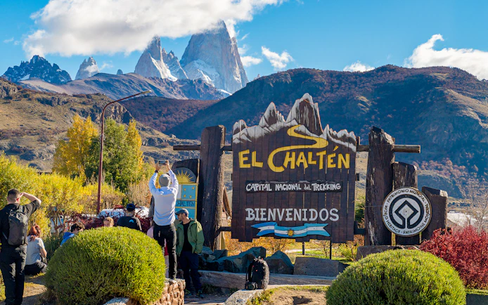 Tourists at El Chaltén welcome sign with mountains in the background, Argentina.