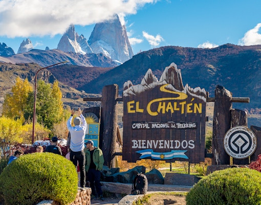 Tourists at El Chaltén welcome sign with mountains in the background, Argentina.