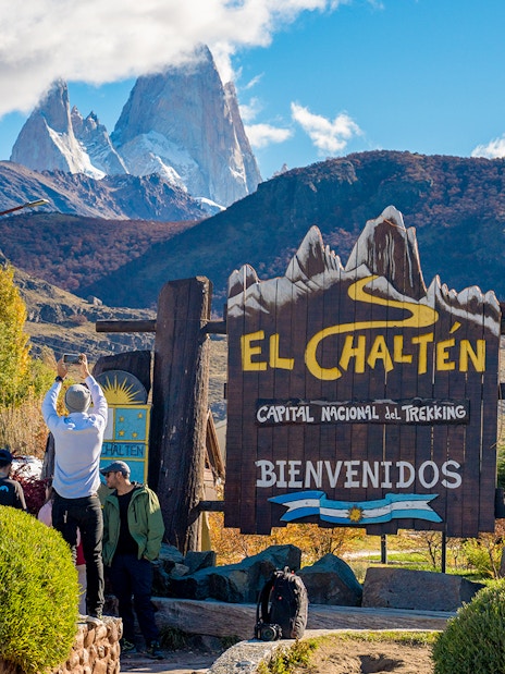 Tourists at El Chaltén welcome sign with mountains in the background, Argentina.