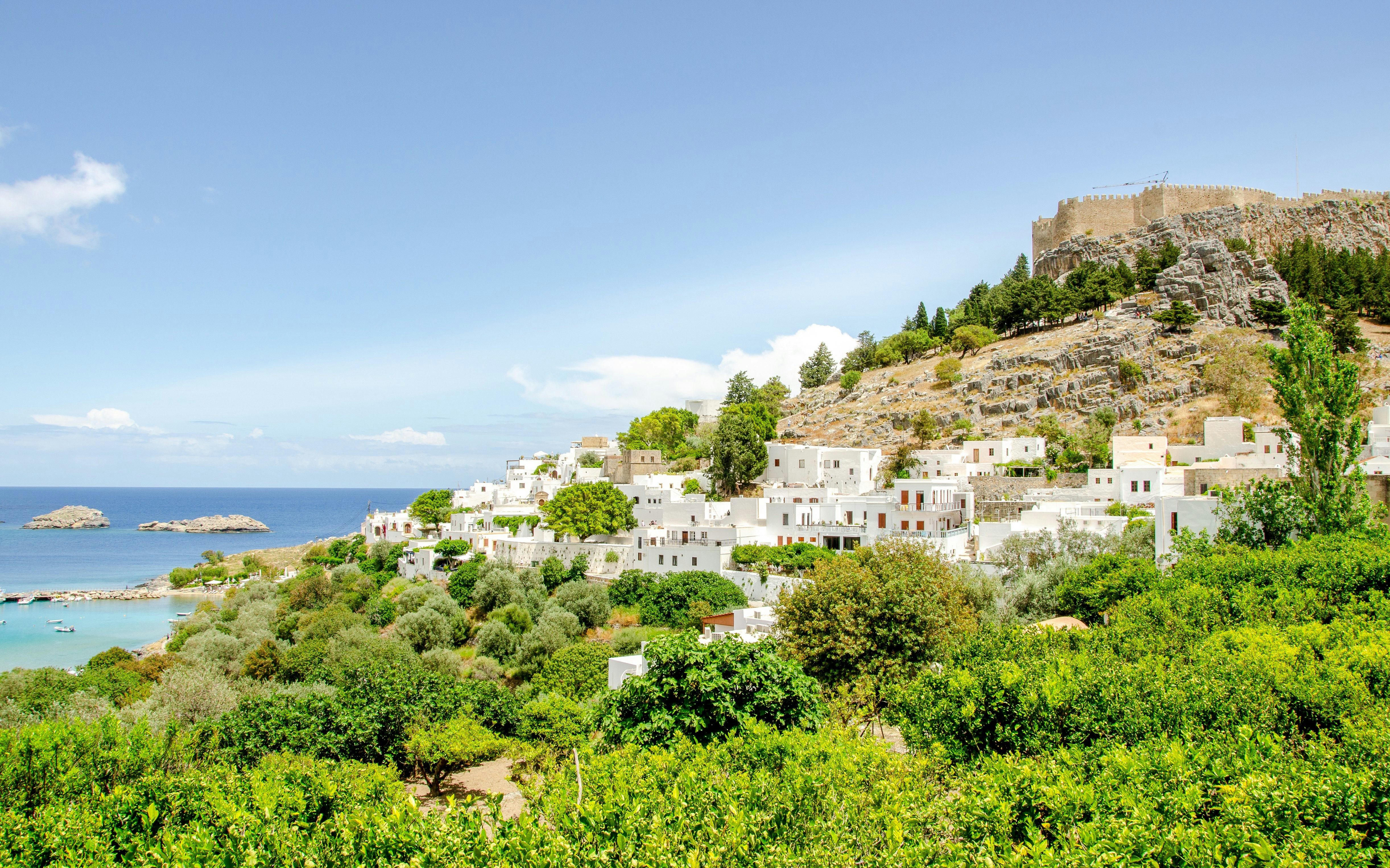 White buildings and lush greenery in Gordes village with a hilltop fortress in the background.