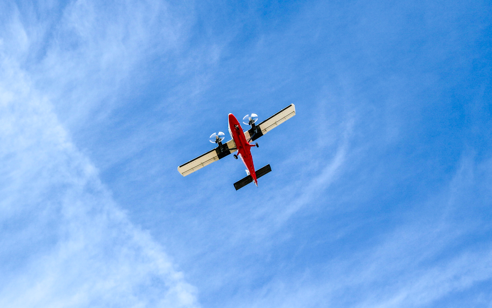 Red airplane flying overhead against a blue sky.