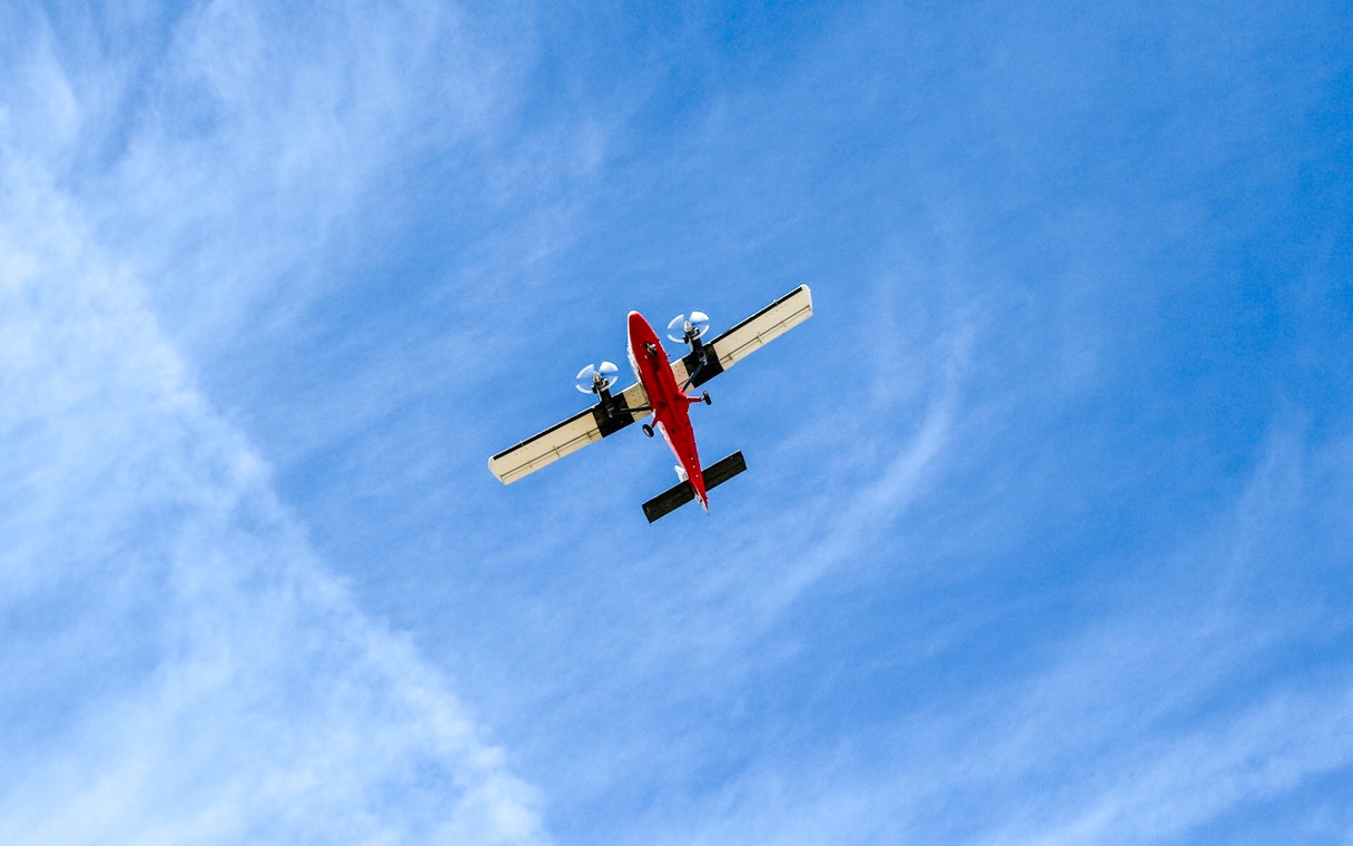 Red airplane flying overhead against a blue sky.