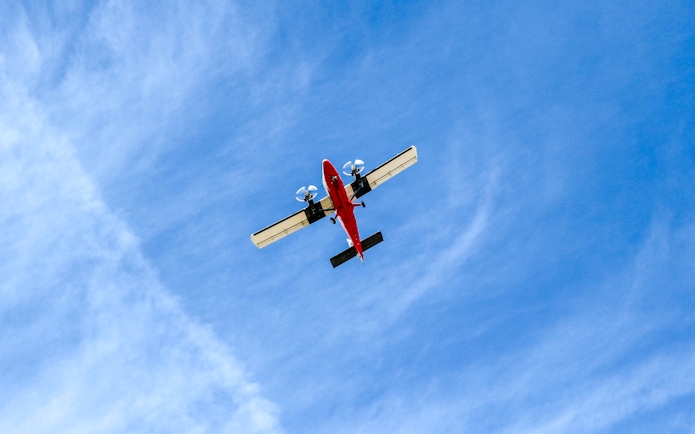 Red airplane flying overhead against a blue sky.