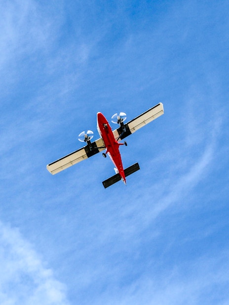 Red airplane flying overhead against a blue sky.