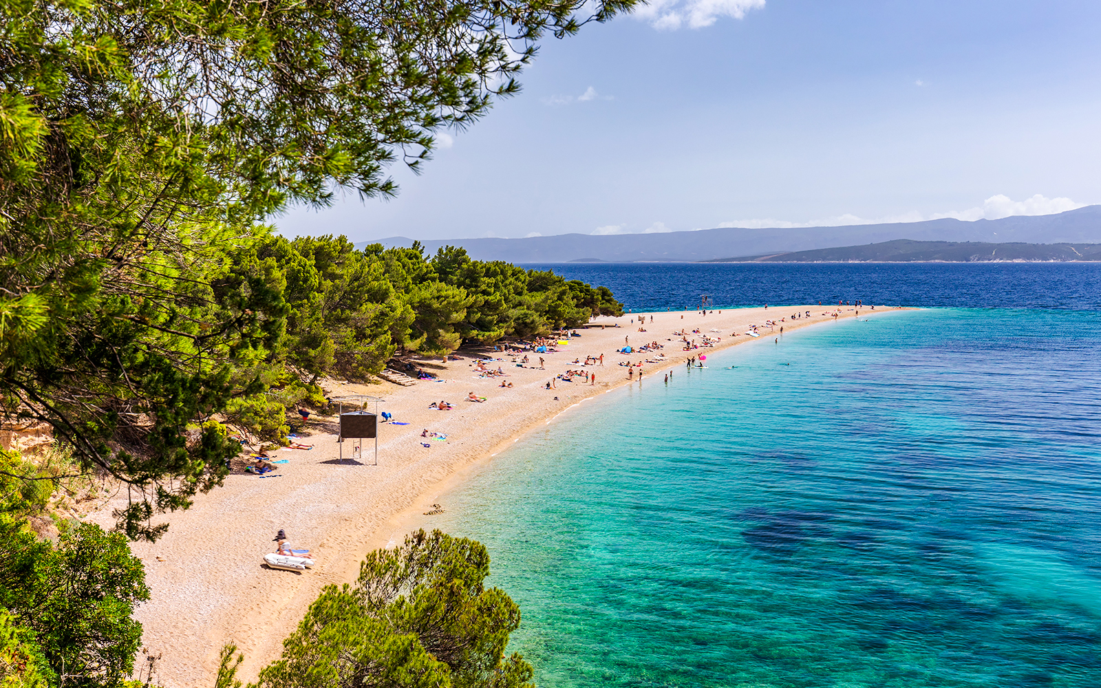 Golden Horn beach in Croatia with turquoise waters and sunbathers on the sandy shore.