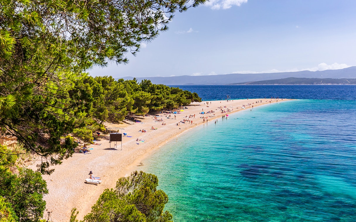 Golden Horn beach in Croatia with turquoise waters and sunbathers on the sandy shore.