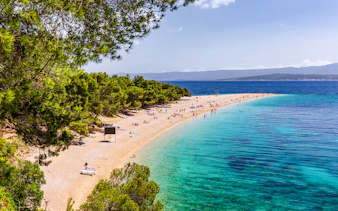 Golden Horn beach in Croatia with turquoise waters and sunbathers on the sandy shore.
