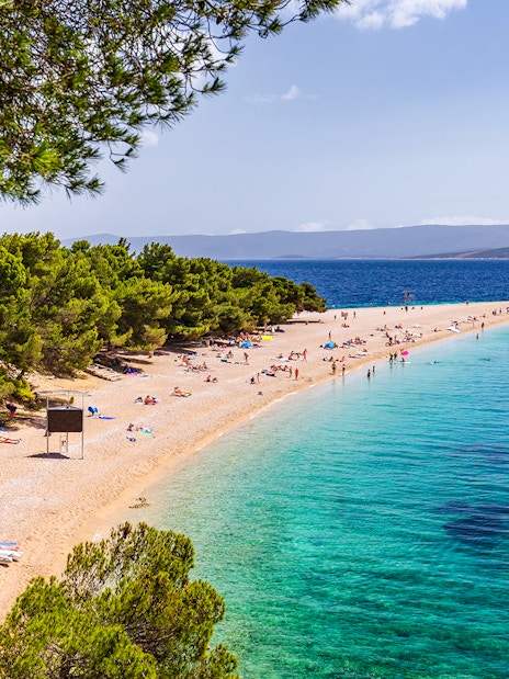 Golden Horn beach in Croatia with turquoise waters and sunbathers on the sandy shore.