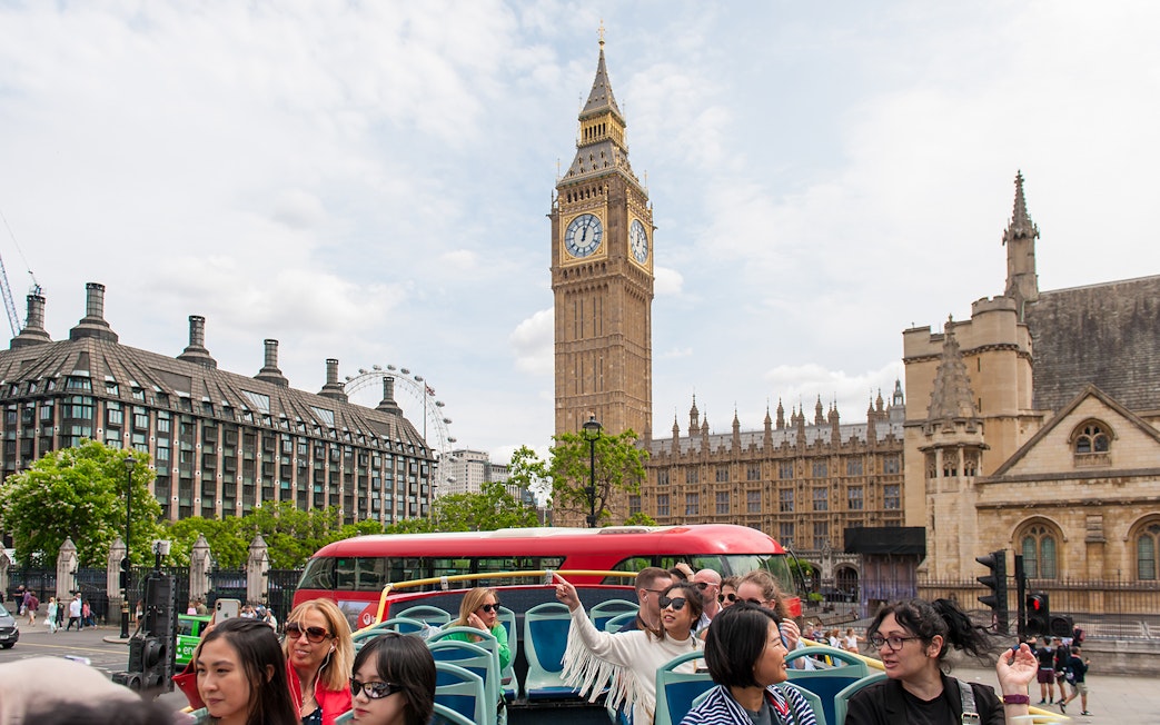 Children on a double-decker bus tour in London, passing Big Ben and the Houses of Parliament.
