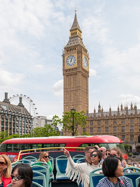 Children on a double-decker bus tour in London, passing Big Ben and the Houses of Parliament.