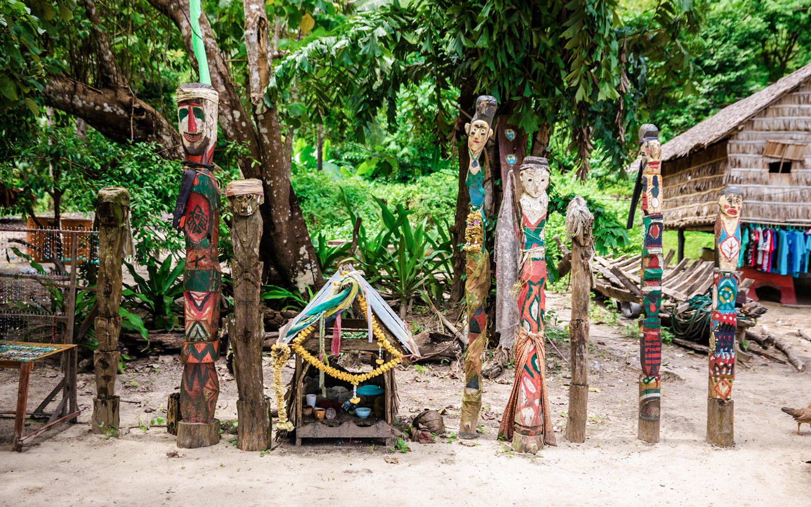 Colorful wooden totems and small shrine in Moken village interior, surrounded by lush greenery.