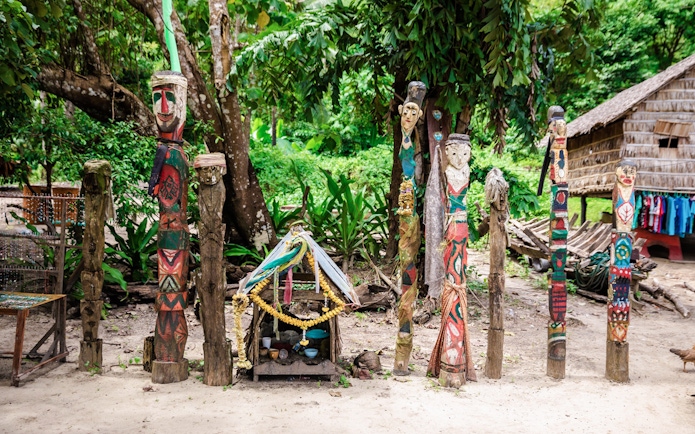 Colorful wooden totems and small shrine in Moken village interior, surrounded by lush greenery.