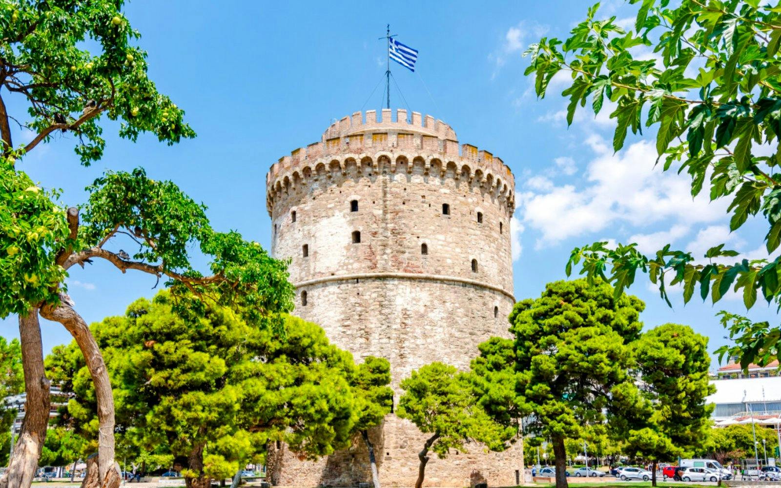 White Tower of Thessaloniki surrounded by trees under a blue sky, Greece.