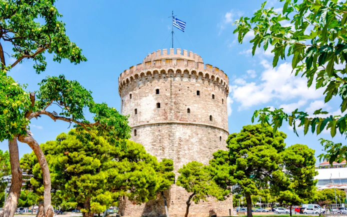 White Tower of Thessaloniki surrounded by trees under a blue sky, Greece.