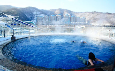 Thermal bath with swimmers at Vivaldi Park Ski World, snowy mountains in the background.
