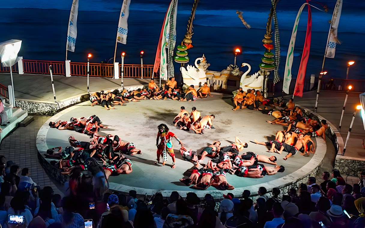 Kecak and Fire Dance performance at Melasti Beach amphitheater, Bali, with dancers in a circle.