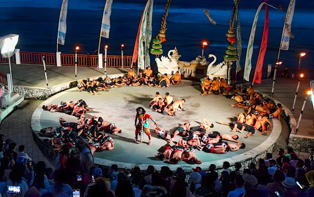 Kecak and Fire Dance performance at Melasti Beach amphitheater, Bali, with dancers in a circle.
