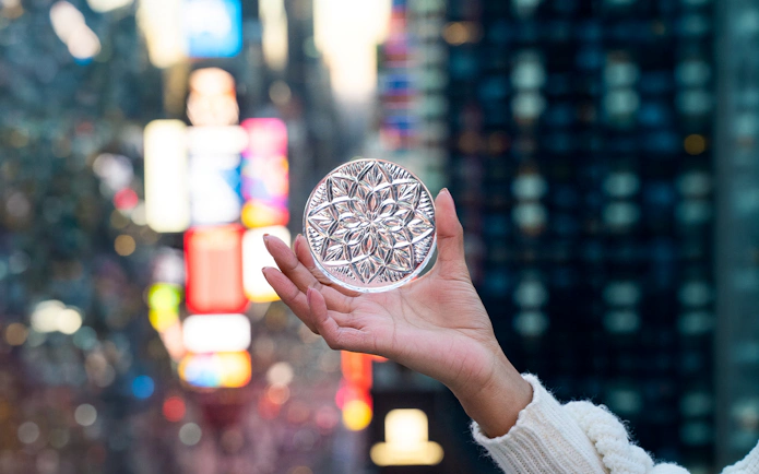 Hand holding a decorative glass disc with Times Square lights in the background.
