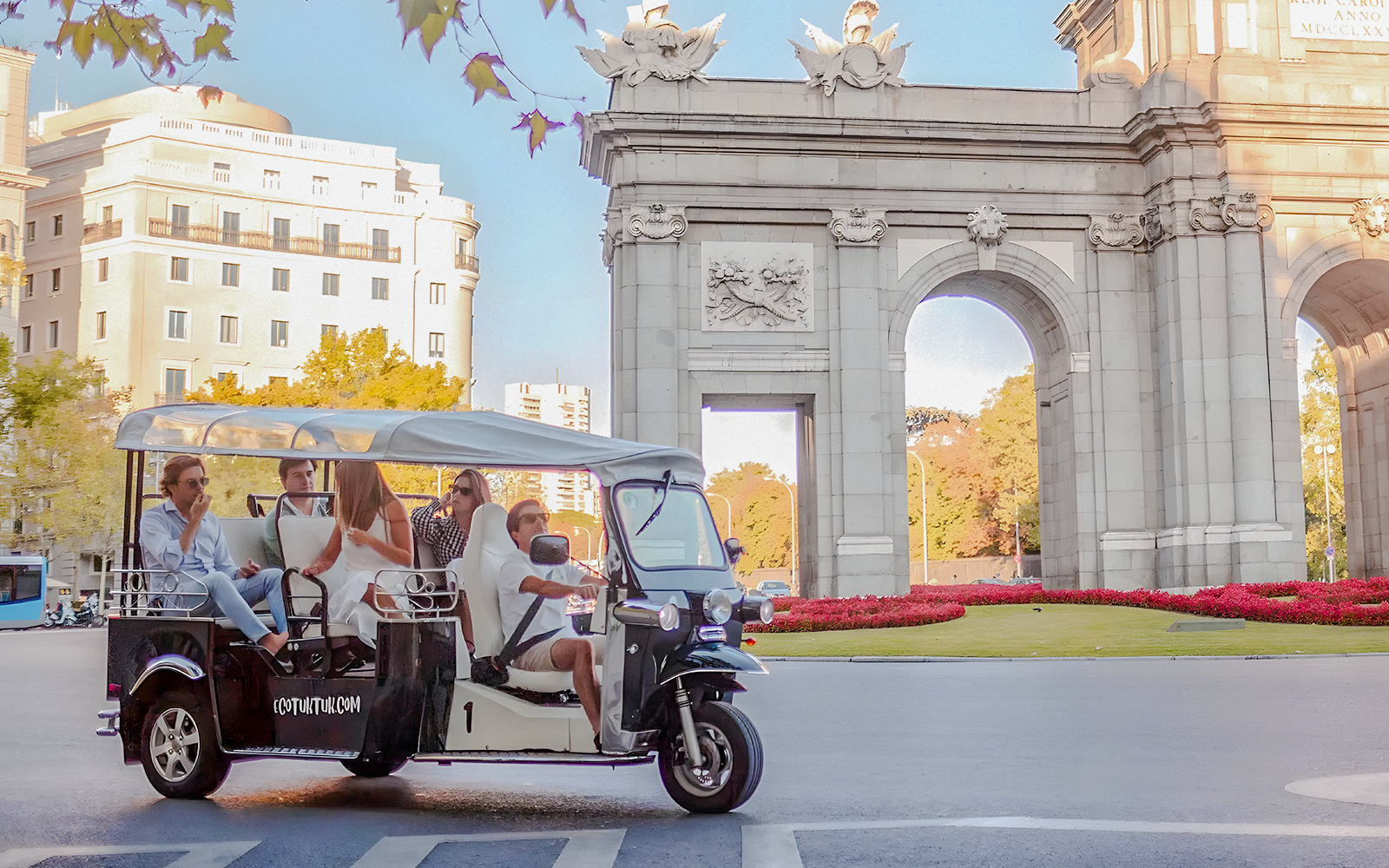 Electric tuk-tuk tour passing Puerta de Alcalá in Madrid, Spain.