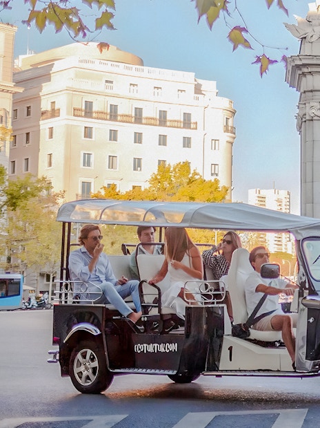 Electric tuk-tuk tour passing Puerta de Alcalá in Madrid, Spain.