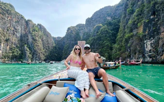 Couple on a decorated long-tail boat in turquoise waters, surrounded by cliffs in Koh Phi Phi, Krabi.