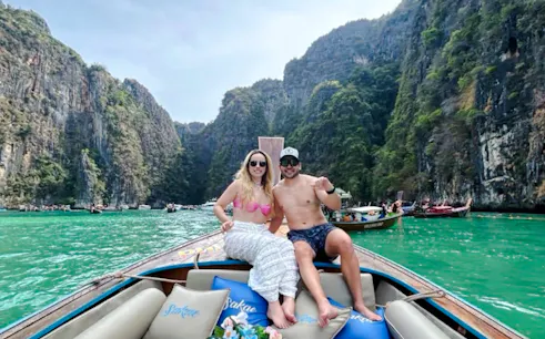 Couple on a decorated long-tail boat in turquoise waters, surrounded by cliffs in Koh Phi Phi, Krabi.