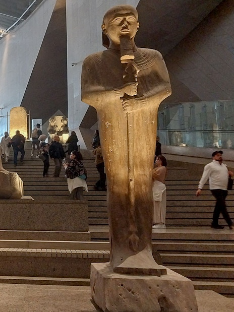 Statues inside the Grand Egyptian Museum with visitors exploring the exhibits.