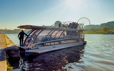 Vistula River cruise boat docked with ferris wheel in background, Krakow, Poland.