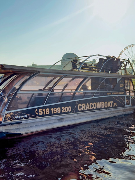 Vistula River cruise boat docked with ferris wheel in background, Krakow, Poland.