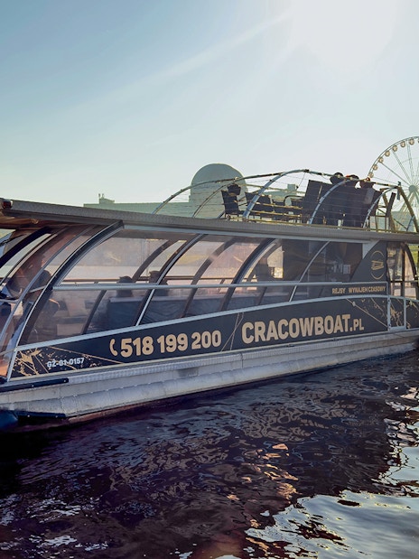 Vistula River cruise boat docked with ferris wheel in background, Krakow, Poland.