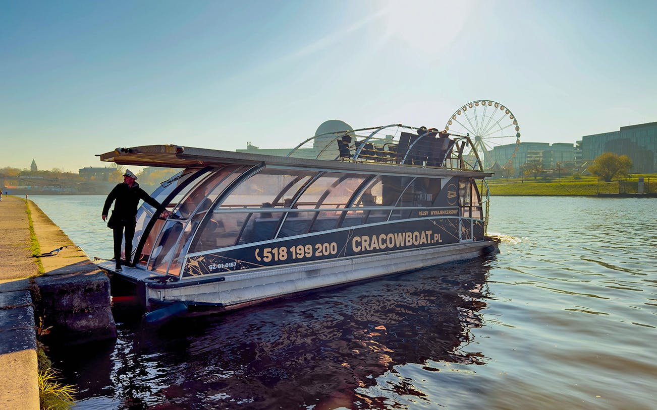Vistula River cruise boat docked with ferris wheel in background, Krakow, Poland.