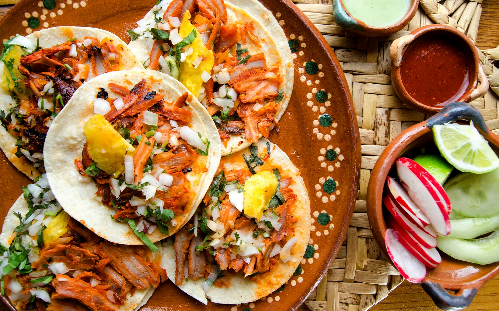 Traditional tacos al pastor with pineapple and onions on a decorated plate in Mexico.