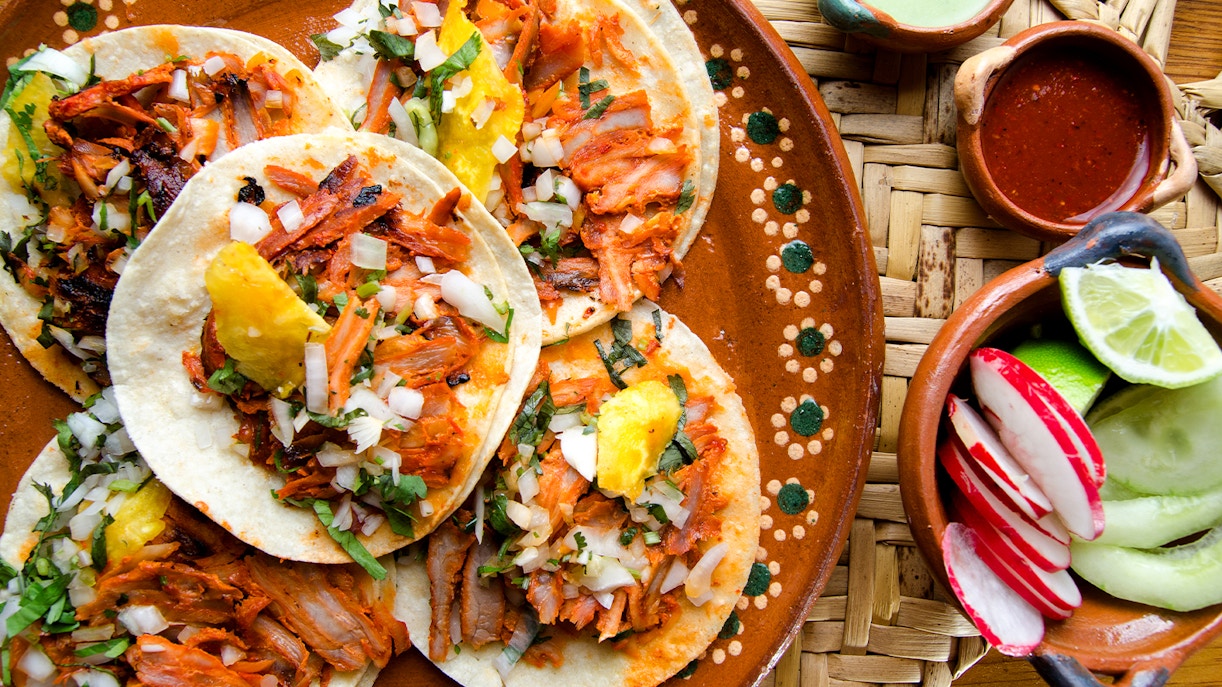 Traditional tacos al pastor with pineapple and onions on a decorated plate in Mexico.