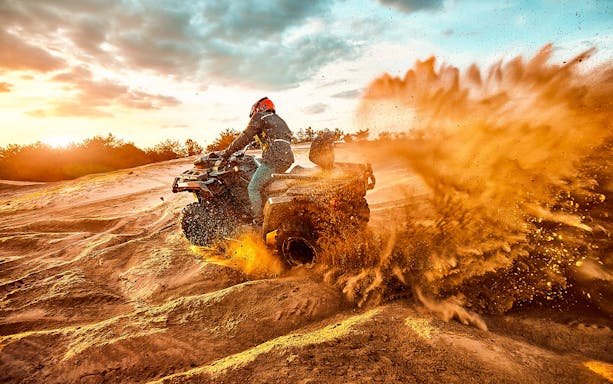 Quad bike kicking up sand on a guided tour in Bosa at sunset.