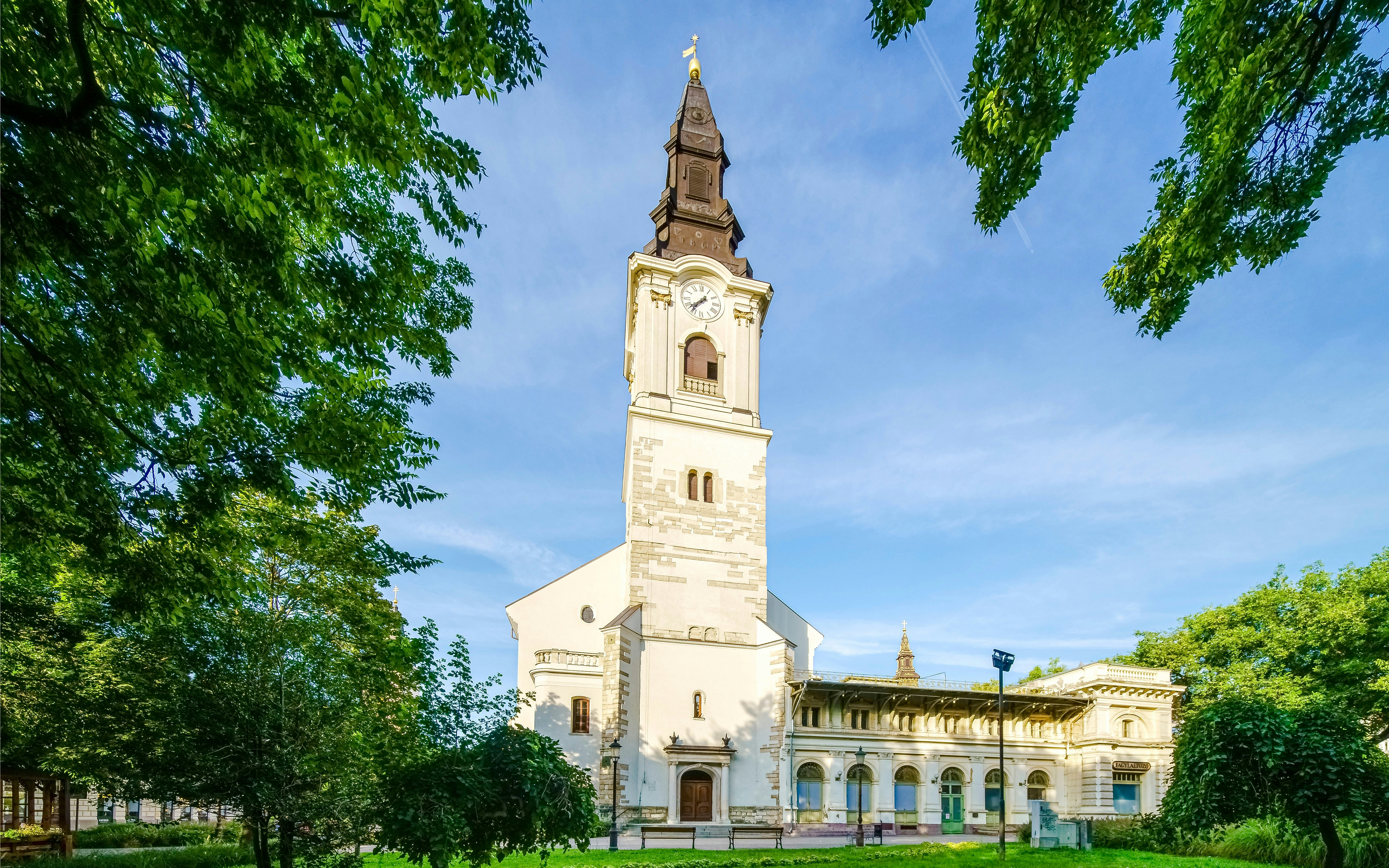 Church in Szabadsag Square, Kecskemet city, surrounded by trees and clear sky.