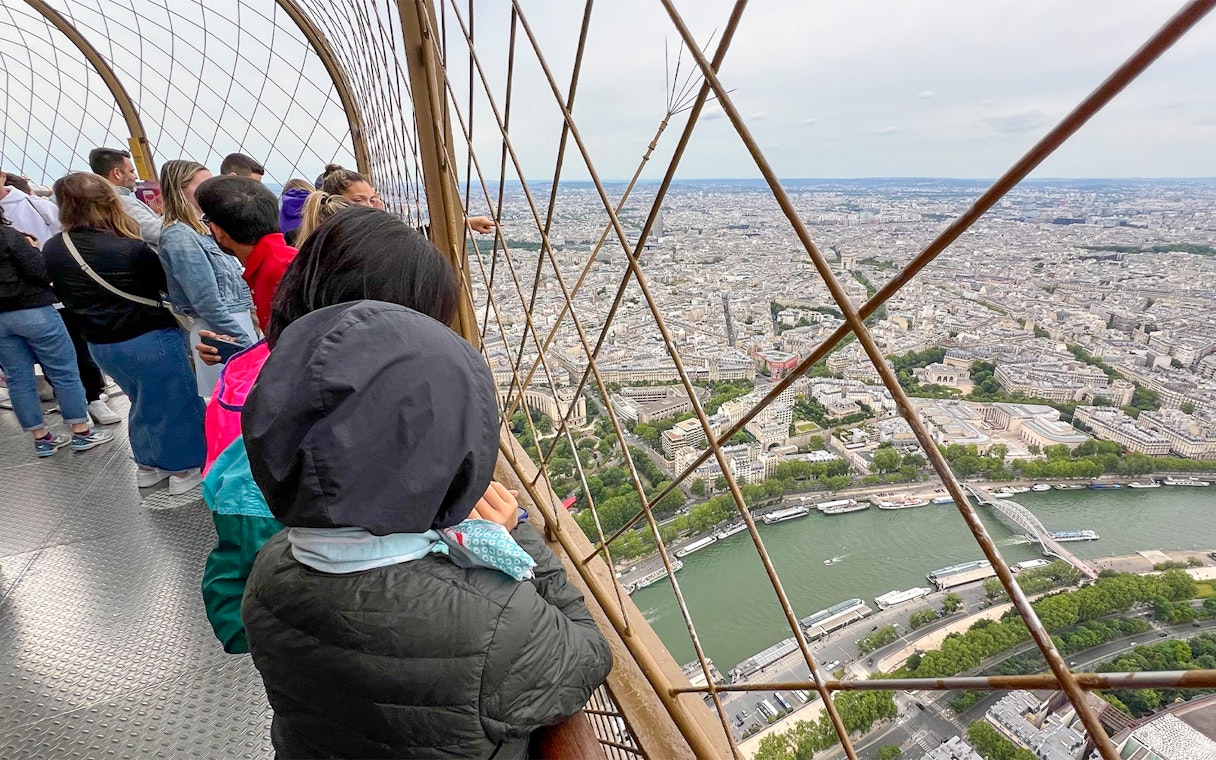Visitors enjoying the view from the Eiffel Tower summit in Paris, overlooking the Seine River.