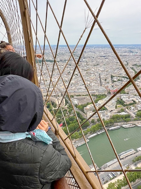 Visitors enjoying the view from the Eiffel Tower summit in Paris, overlooking the Seine River.