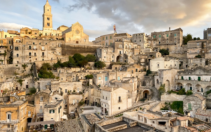 Matera's ancient stone buildings and church under a cloudy sky during a 2-hour guided tour.