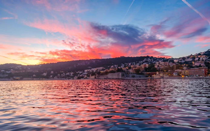 Villefranche coastline at sunset during a boat tour, vibrant sky reflecting on water.