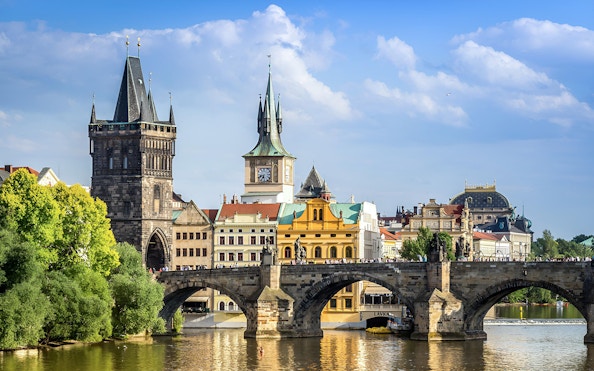 Charles Bridge over Vltava River in Prague with historic towers and buildings in the background.