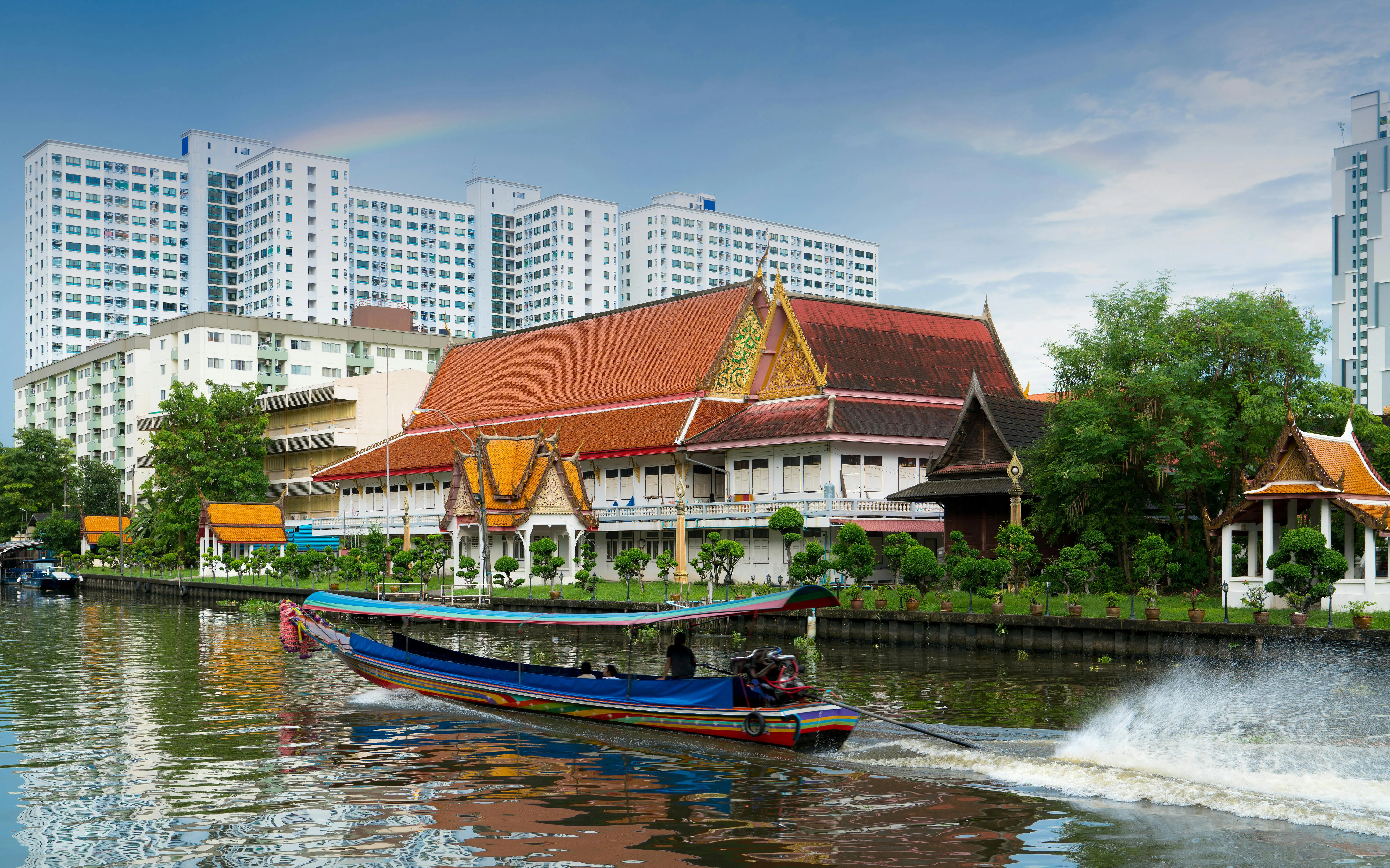 Longtail boat on Khlong Ban Pa with Wat Tai Temple, Bangkok residential area in background.