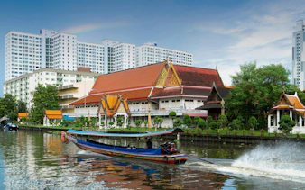 Longtail boat on Khlong Ban Pa with Wat Tai Temple, Bangkok residential area in background.