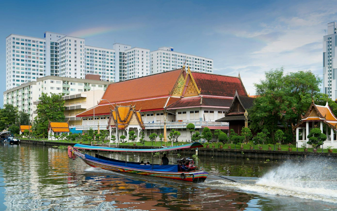 Longtail boat on Khlong Ban Pa with Wat Tai Temple, Bangkok residential area in background.
