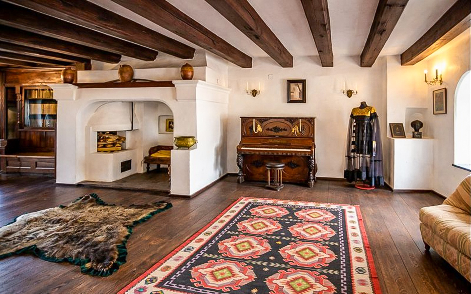Bran Castle interior with wooden beams, a piano, traditional rug, and historical decor in Romania.