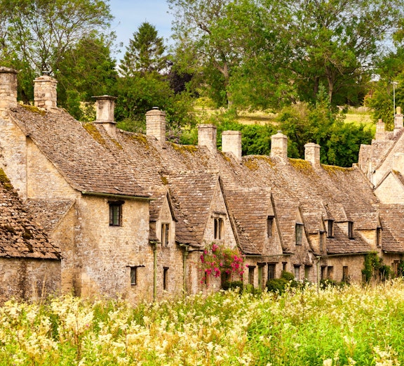 Row of historic stone cottages in Cotswold, surrounded by lush greenery.