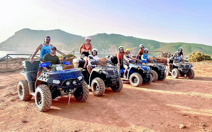 Tourists on quad bikes during an excursion in Alghero with scenic mountain backdrop.