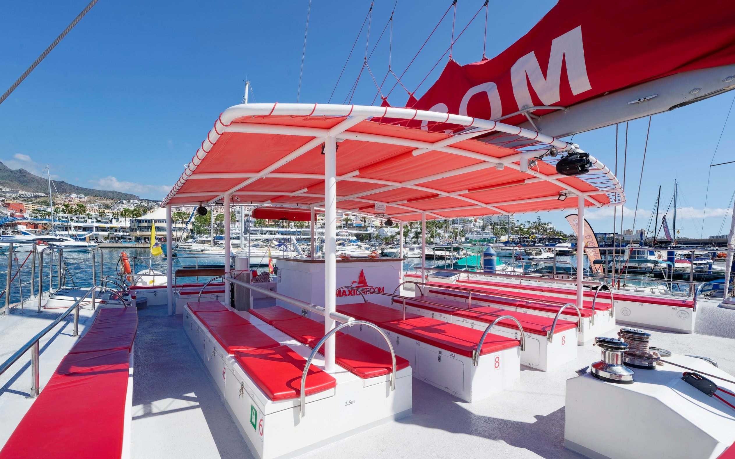 Tourist boat docked at the port of Tenerife Costa Adeje with red seating and canopy.