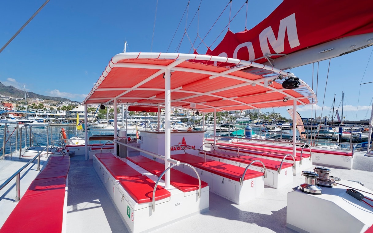 Tourist boat docked at the port of Tenerife Costa Adeje with red seating and canopy.